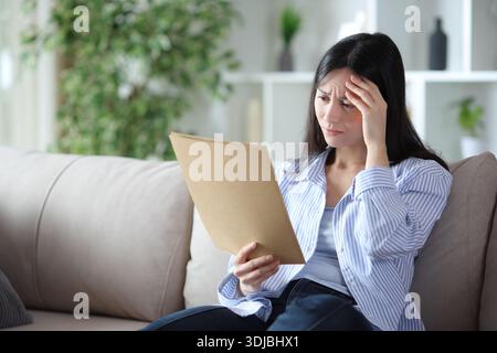 Worried asian woman checking documents sitting on a sofa at home Stock Photo