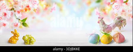 Pastel Easter scene featuring ceramic bunnies, decorated eggs with ribbons, and a floral hen figurine set against soft cherry blossoms Stock Photo
