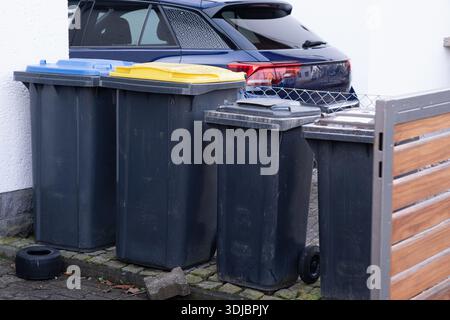Row of color-coded recycling bins (paper, plastic/metal, residual waste) outside a home. Highlights efficient waste management, sustainability, and ty Stock Photo