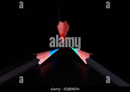Three Colored Pencils Meeting at One Point on Black Background Stock Photo