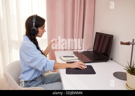 Woman wearing headphones and using laptop for online conference Stock Photo