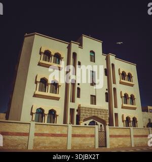 A low-angle shot of a traditional Omani building featuring arched windows with intricate details, a decorative gate, and a textured wall. The cream-co Stock Photo