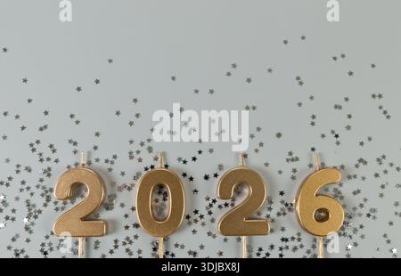 2026 Happy New Year. Top view of gold numbers, silver stars confetti on grey background. Copy space, flat lay. Stock Photo