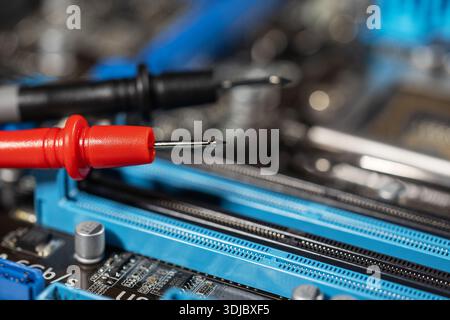 red and black multimeter probe probing electric components on circuit board. Diagnostic testing in technical laboratory setting Stock Photo