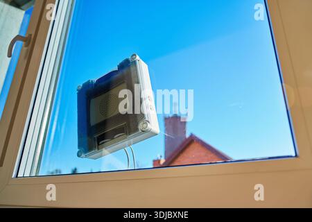 Square window cleaning robot washing glass. Robotic window cleaner working on window surface against blue sky. Smart home appliance concept Stock Photo