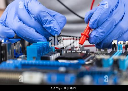 Technician repairs computer motherboard with multimeter and tools in workshop setting. Stock Photo