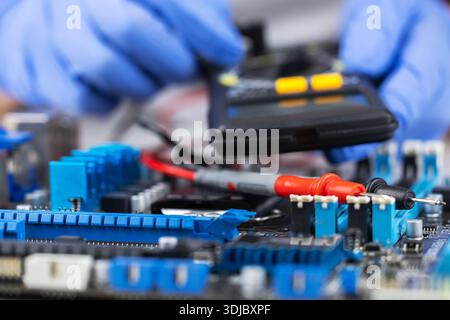 Testing motherboard with probes and multimeter, Close-up of technician using probes on computer motherboard with red multimeter during electronic diag Stock Photo