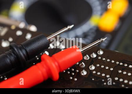 red and black multimeter probe probing electric components on circuit board. Diagnostic testing in technical laboratory setting Stock Photo