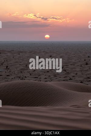 Stunning sunset over the vast Oman desert, featuring a large sun and beautiful pink and orange clouds. Ideal for travel, nature, and adventure-themed Stock Photo
