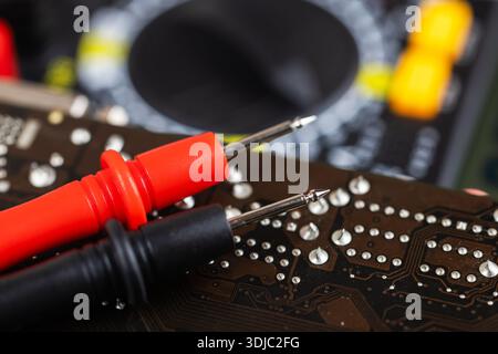 Testing motherboard with probes and multimeter, Close-up of technician using probes on computer motherboard with red multimeter during electronic diag Stock Photo