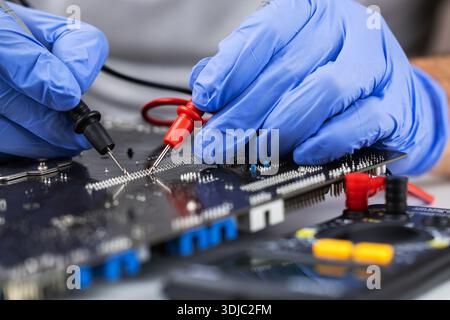 Testing motherboard with probes and multimeter, Close-up of technician using probes on computer motherboard with red multimeter during electronic diag Stock Photo