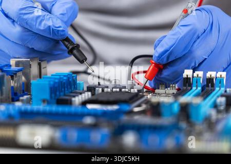 Testing motherboard with probes and multimeter, Close-up of technician using probes on computer motherboard with red multimeter during electronic diag Stock Photo