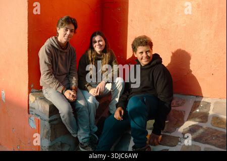 Group of three young friends relax by an orange wall Stock Photo