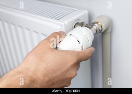 male's hand adjusting radiator temperature using thermostat. Home with central heating. Stock Photo