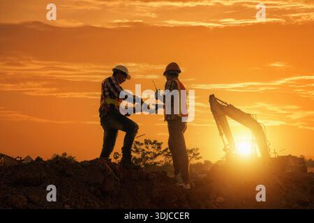 Side view of Two Engineers talking to each other on a building site at sunset, Thailand Stock Photo