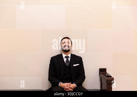 Portrait of a smiling businessman in a suit sitting on a bench next to his mobile phone and sunglasses with his eyes closed Stock Photo