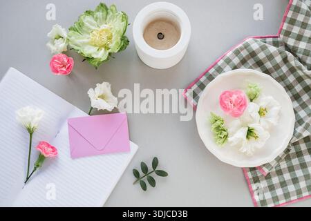 Close-up overhead view of assorted flowers, a candle, blank envelope and open notebook on a table Stock Photo