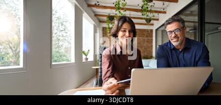 Two happy busy male and female business people working at desk using laptop. Stock Photo