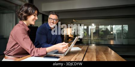 Business team two happy workers working together using laptop sitting in office. Stock Photo