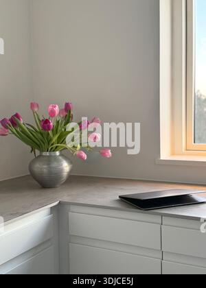 Close-up of a laptop computer on a kitchen worktop next to a vase with pink tulips Stock Photo