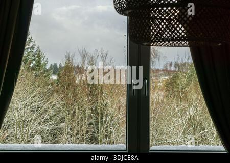 A winter landscape with snow covered trees seen through a home window from inside a cozy interior. Stock Photo