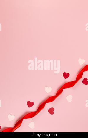 Top view of red ribbon, red hearts and pink hearts on pink background. Valentine's day, love. Shiny rolled fabric, silk and satin material. Copy space. Stock Photo