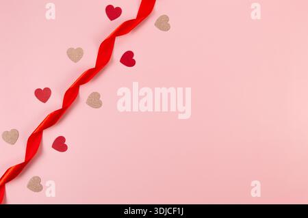 Top view of red ribbon, red hearts and pink glitter hearts on pink background. Valentine's day, love. Shiny rolled fabric, silk and satin material. Stock Photo