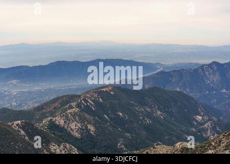 Scenic landscape of layered, blue mountain ridges fading into a hazy horizon, overlooking a sprawling urban valley in the San Gabriel Mountains, Calif Stock Photo