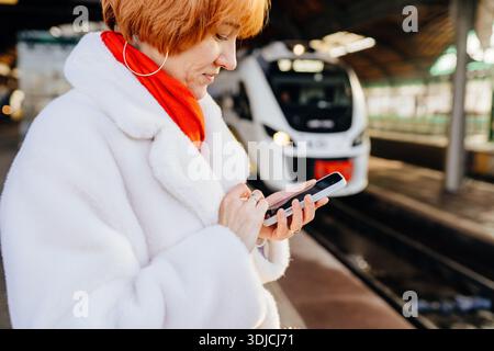 Caucasian redhead woman using smartphone on railway platform Stock Photo