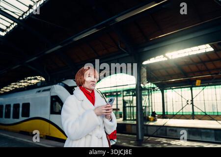 Caucasian redhead woman using smartphone while waiting for train at station Stock Photo