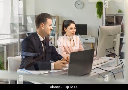 Colleagues at computer and laptop discussing finance planning in modern office Stock Photo
