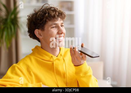 Young man in yellow hoodie using smartphone speakerphone at home Stock Photo