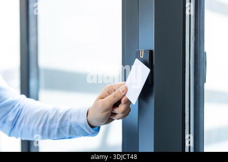 Hand holding white access card to an rfid reader, unlocking an electronic office door for secure, contactless entry and employee identification in a modern corporate building Stock Photo