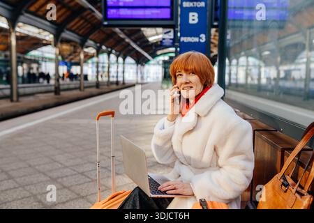 Confident middle aged caucasian redhead woman making business call at train station Stock Photo