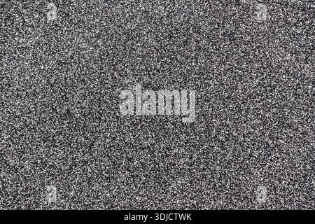 Dark granular asphalt or gravel surface with dense stone texture, suitable as abstract industrial or construction background Stock Photo