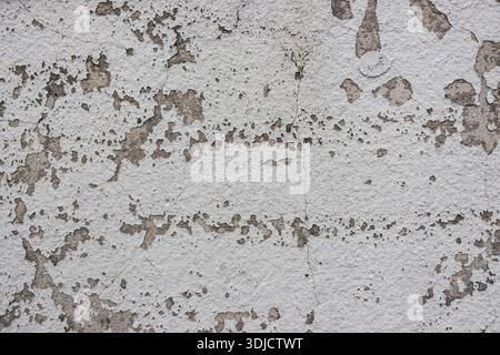 Severely weathered wall with peeling paint and exposed plaster creating a gritty, distressed texture background Stock Photo
