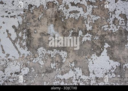 Severely weathered wall with peeling paint and exposed plaster creating a gritty, distressed texture background Stock Photo