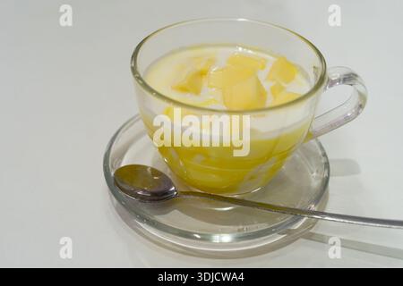 A glass cup filled with smooth mango yogurt, topped with freshly cut pieces of ripe mango Stock Photo