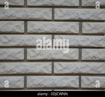 Close-up view of an empty white brick wall with a clean, repetitive masonry pattern. Textured white and grey small stone or granite bricks. Stock Photo