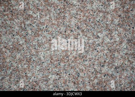 Close-up of a natural marble or granite stone surface with fine speckled texture and neutral gray and brown, orange tones. Detailed rock pattern. Stock Photo