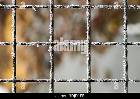 A metal fence covered in snow. The fence is made up of many small squares. The snow is covering the fence in a way that it looks like a pattern Stock Photo