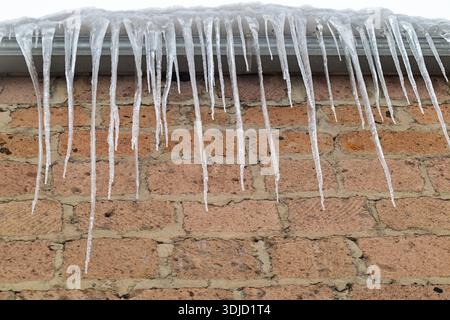 A brick wall covered in icicles. The icicles are long and thin, and they are hanging from the roof. The scene has a cold and wintry mood, with the ici Stock Photo
