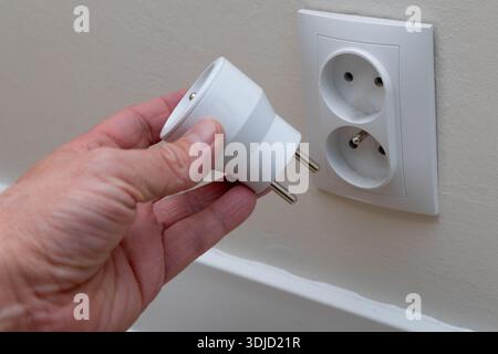 A man plugs a plug into a socket, a man's hand inserting a plug into the holes of a smart socket, an electrical outlet controlled by a phone, a smart Stock Photo