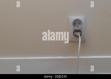 Plug plugged into an electrical outlet, smart electrical outlet, electrical outlet on a white wall in a room Stock Photo