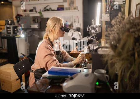 Craftswoman examining details using a microscope in workshop Stock Photo