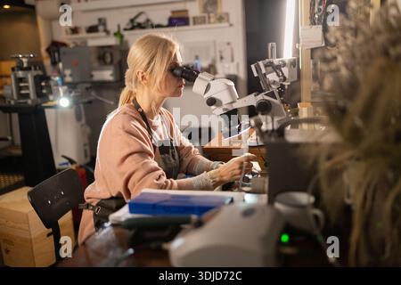 Woman examining jewelry details using microscope in workshop Stock Photo