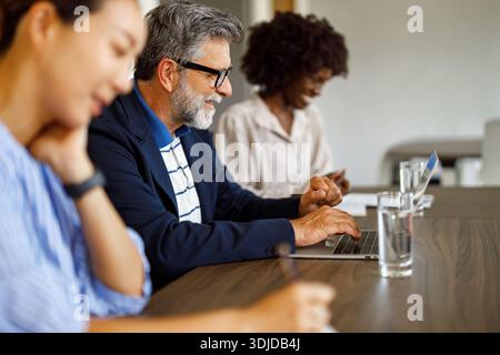 Smiling male lawyer using laptop while discussing strategy with female colleagues during meeting in conference room Stock Photo