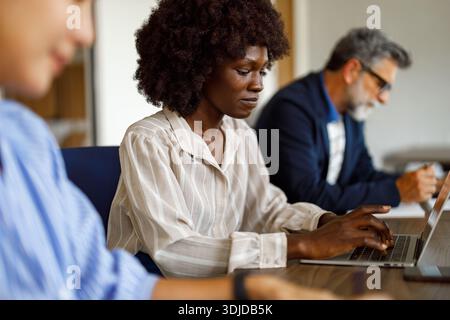 Focused accountant analyzing report on laptop while collaborating with colleagues in modern office workspace Stock Photo