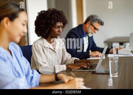 Focused businesswoman typing on laptop and analyzing data while working with colleagues in modern office Stock Photo