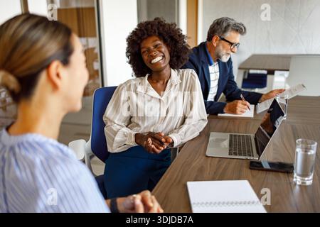 Cheerful female professionals talking while mature businessman reviewing financial report in background in modern office Stock Photo